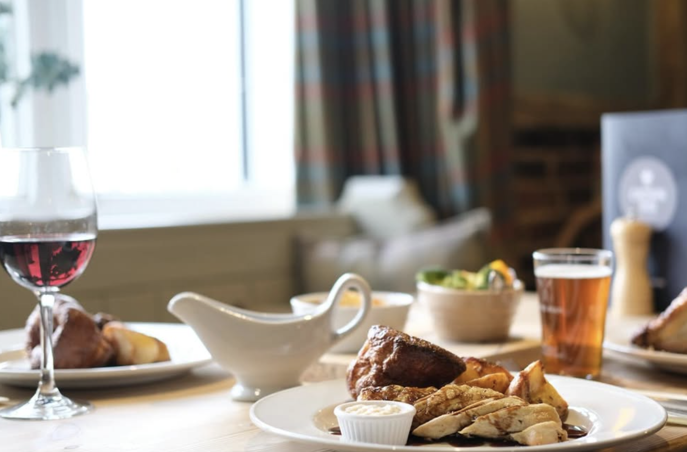 Sunday roast on the table with red wine, gravy boat and a pint of ale